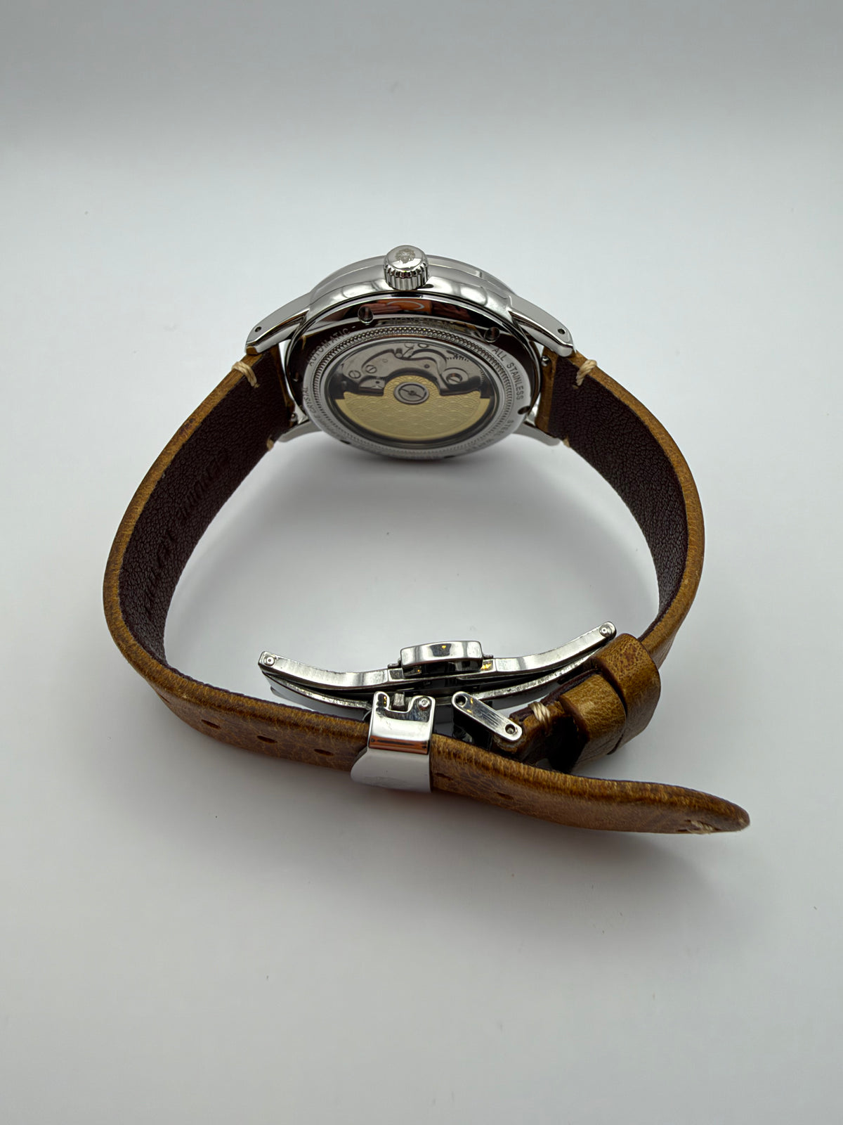 Ethos GMT rear view showing a display caseback, plain gold-tone rotor and brown strap with folding clasp.
