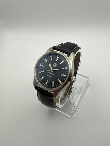 Resolute at an angle, with a dark striped dial, silver-tone case and black strap with white stitching.