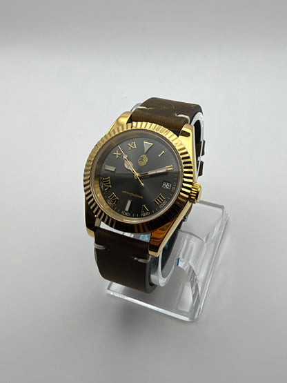 Auctor at an angle, with a dark Roman-numeral dial, gold-tone fluted bezel and brown strap.