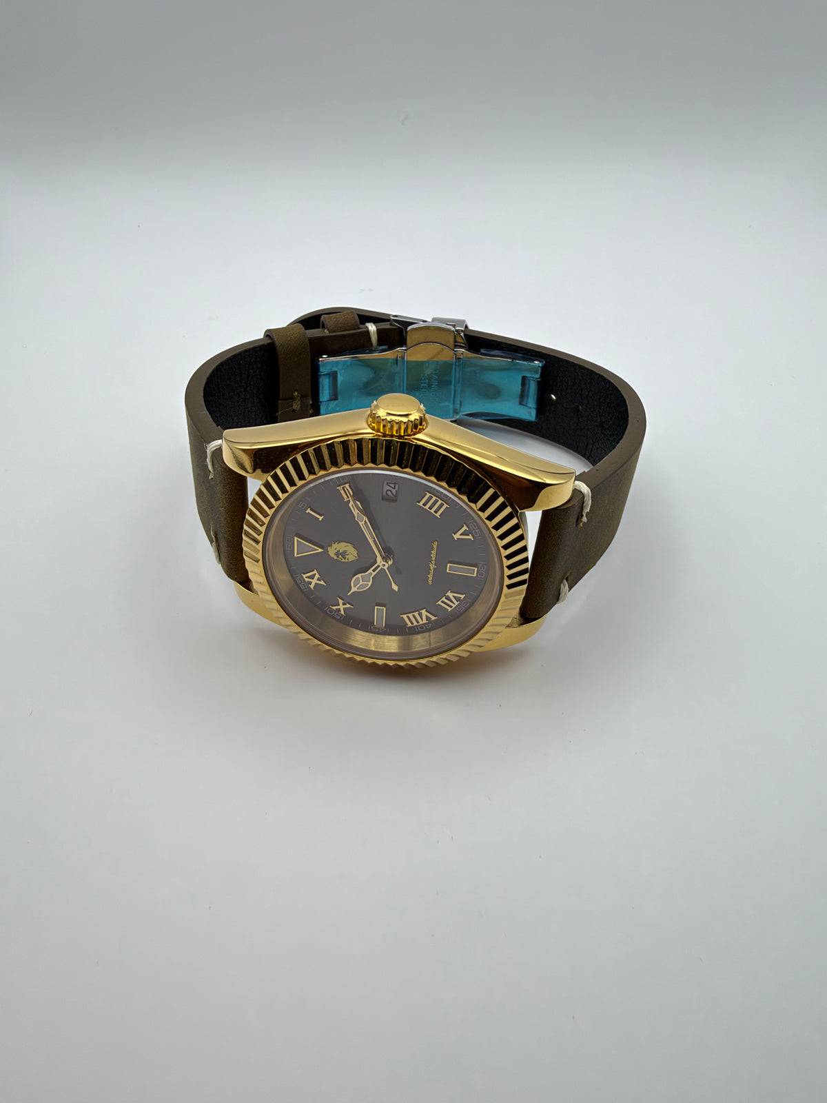 Auctor resting at an angle, showing the gold-tone case, brown strap and blue film on the clasp.