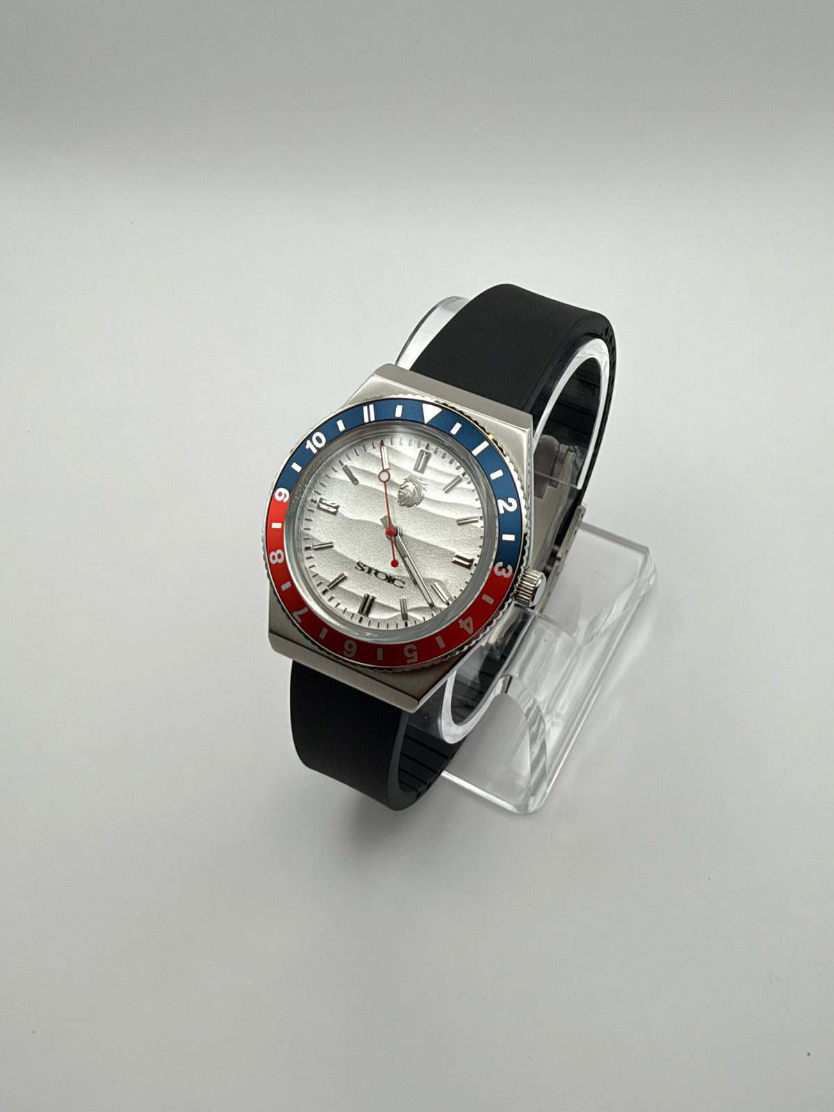 Voyager at an angle, with a white textured dial, red and blue bezel, and black strap.