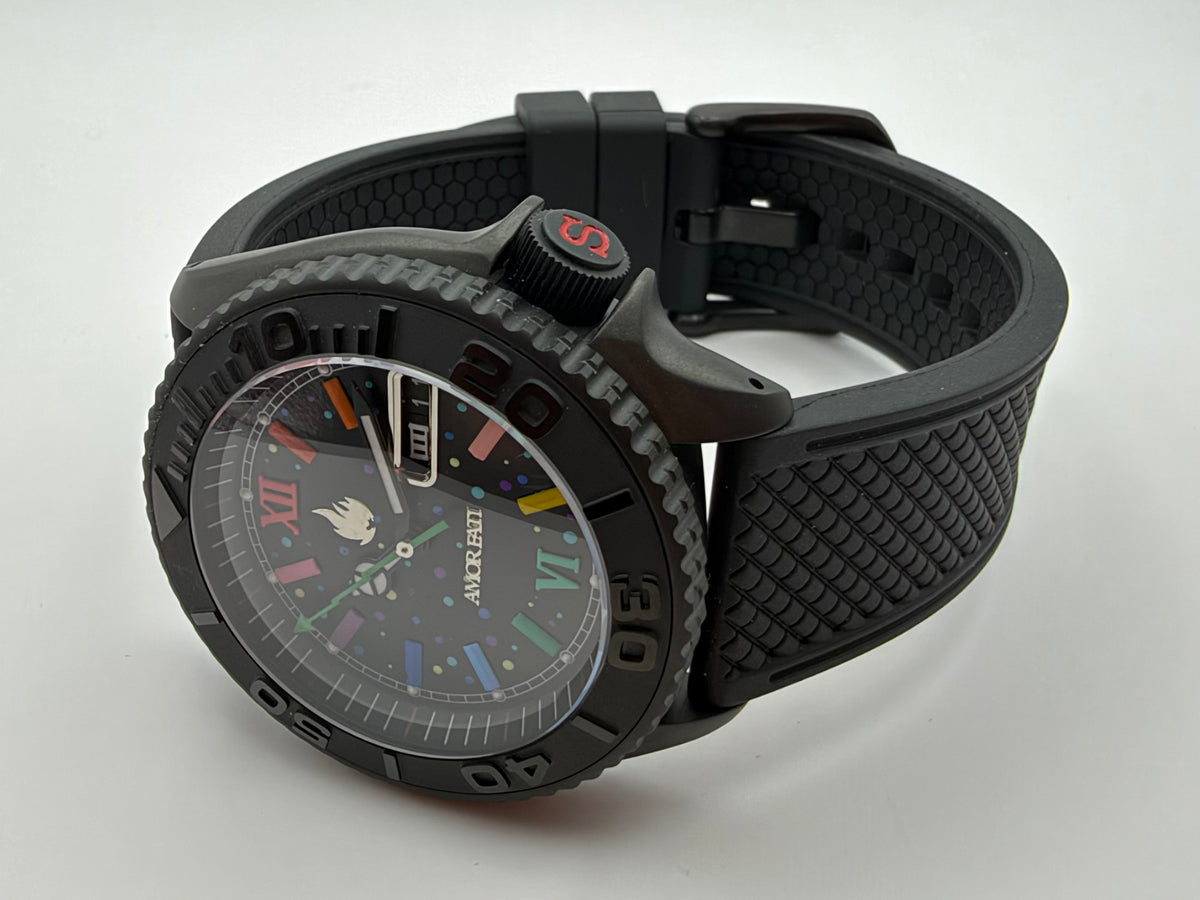 Black watch with multicolor markers and AMOR FATI on the dial, resting beside its textured black strap.