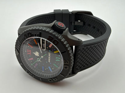 Black watch with multicolor markers and AMOR FATI on the dial, resting beside its textured black strap.